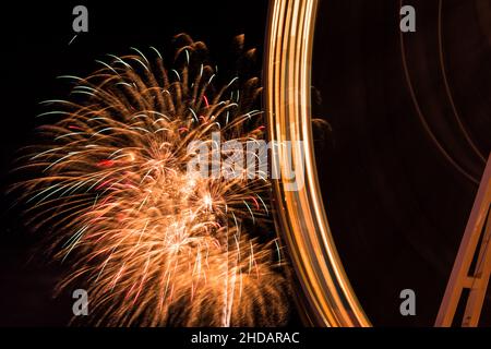 Schöne Aufnahme von Feuerwerken, die am dunklen Himmel mit Fähren-Rad im Vordergrund strahlen Stockfoto