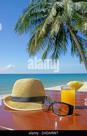 Sonnenhut mit Sonnenbrille und Fruchtsaft unter Palmen am Strand in Thailand Stockfoto