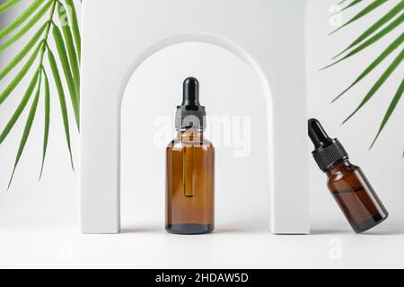 Tropfflaschen aus Glas mit einer Pipette mit schwarzer Gummispitze und grünen Blättern in der Nähe auf weißem Hintergrund. Naturhautkonzept. Organische Spa-Kosmetik Stockfoto