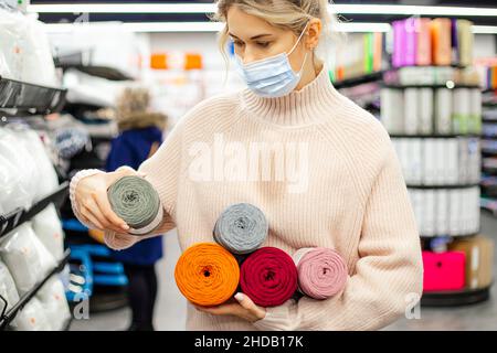 Frau, die mit Handarbeiten beschäftigt ist, liest sorgfältig die Komposition aus Wollknäuel und hält mehrfarbige Knäuel in den Händen. Einkaufen. Garnlager. Kunsthandwerk und Stockfoto