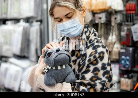 Schöne junge Frau in Maske hält Anti - Stress Hund Spielzeug in den Händen. Department of Home Goods Hypermarket. Linderung von Stress und Angst in Pandemi Stockfoto