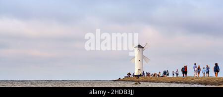 Touristen laufen auf dem Pier zu einem Leuchtturm an der Ostsee in Swinoujscie in Polen. Mit verschwommenem bewölktem Himmel im Hintergrund. Stockfoto