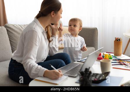 Mütter können Arbeit und Familie in Einklang bringen. Junge Mutter multitasking und arbeitet von zu Hause aus und verbringt Zeit mit dem Sohn Stockfoto