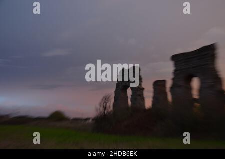 Fotos, die bei Sonnenuntergang bei einem Spaziergang durch den wunderschönen Aquädukt-Park in Rom mit den majestätischen Ruinen der antiken römischen Aquädukte und Bäume aufgenommen wurden Stockfoto