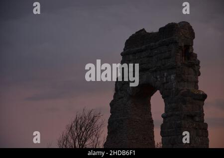 Fotos, die bei Sonnenuntergang bei einem Spaziergang durch den wunderschönen Aquädukt-Park in Rom mit den majestätischen Ruinen der antiken römischen Aquädukte und Bäume aufgenommen wurden Stockfoto