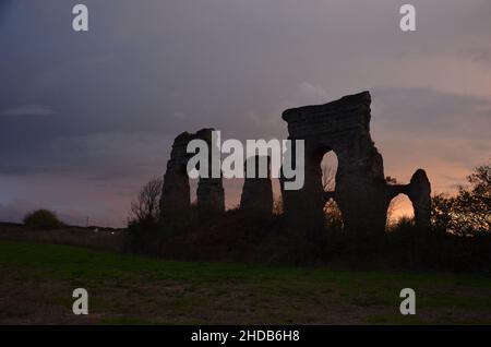 Fotos, die bei Sonnenuntergang bei einem Spaziergang durch den wunderschönen Aquädukt-Park in Rom mit den majestätischen Ruinen der antiken römischen Aquädukte und Bäume aufgenommen wurden Stockfoto