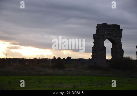 Fotos, die bei Sonnenuntergang bei einem Spaziergang durch den wunderschönen Aquädukt-Park in Rom mit den majestätischen Ruinen der antiken römischen Aquädukte und Bäume aufgenommen wurden Stockfoto