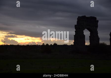 Fotos, die bei Sonnenuntergang bei einem Spaziergang durch den wunderschönen Aquädukt-Park in Rom mit den majestätischen Ruinen der antiken römischen Aquädukte und Bäume aufgenommen wurden Stockfoto