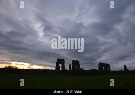 Fotos, die bei Sonnenuntergang bei einem Spaziergang durch den wunderschönen Aquädukt-Park in Rom mit den majestätischen Ruinen der antiken römischen Aquädukte und Bäume aufgenommen wurden Stockfoto