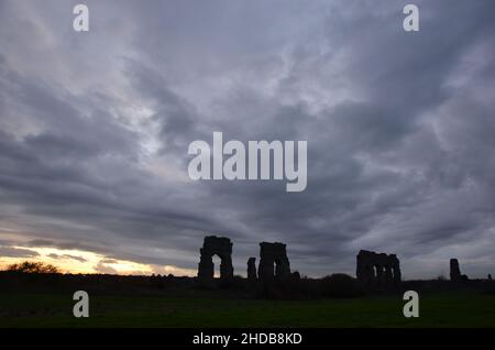 Fotos, die bei Sonnenuntergang bei einem Spaziergang durch den wunderschönen Aquädukt-Park in Rom mit den majestätischen Ruinen der antiken römischen Aquädukte und Bäume aufgenommen wurden Stockfoto