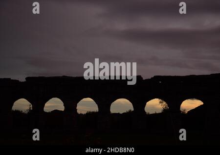 Fotos, die bei Sonnenuntergang bei einem Spaziergang durch den wunderschönen Aquädukt-Park in Rom mit den majestätischen Ruinen der antiken römischen Aquädukte und Bäume aufgenommen wurden Stockfoto