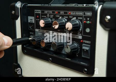 Nahaufnahme der Hand eines Mannes, der eine elektrische Gitarrenbuchse in einen Verstärker einsteckt. Stockfoto