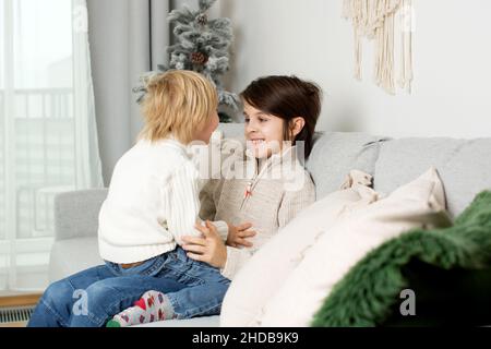 Junge Brüder, umarmt zu Hause auf dem Sofa, Kind kuschelt in älteren Bruder, Ruhe, Glück zusammen in der Familie Stockfoto