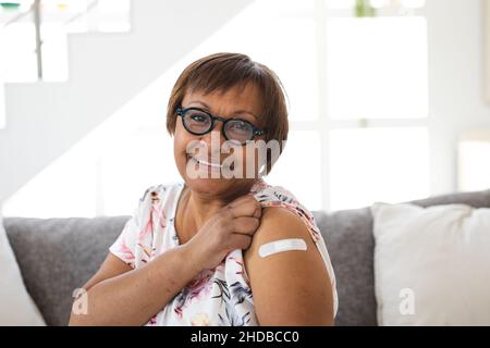 Porträt einer lächelnden älteren Frau, die nach der Impfung einen Haftverband am Arm zeigt Stockfoto