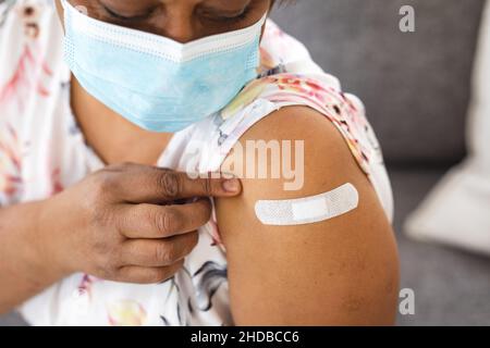 Ältere Frau in einer schützenden Gesichtsmaske, die nach der Impfung eine klebende Bandage am Arm zeigt Stockfoto