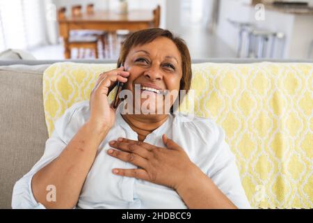 Lächelnde ältere Frau, die zu Hause auf dem Sofa sitzt und auf dem Smartphone spricht Stockfoto
