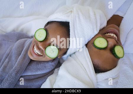 Mutter und Tochter lächelten in Bademänteln, während sie sich mit Gurkenscheiben auf den Augen im Spa erholten Stockfoto