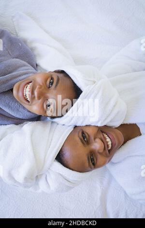 Portrait von fröhlicher Mutter und Tochter in Bademänteln, die sich im Spa auf dem Bett entspannen Stockfoto