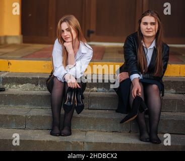 Müde Schülerinnen sitzen barfuß auf den Stufen der Schule. Stockfoto