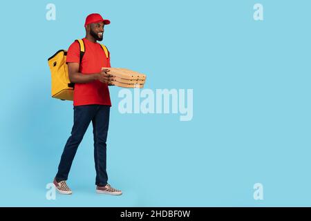 Junger Lächelnder Black Courier Guy Trägt Thermal Backpack Walking Mit Pizzakisten Stockfoto