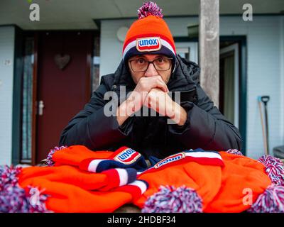 Ein Mann posiert mit einer traditionellen orangen Beanie von Unox. Diese Woche ist es genau 25 Jahre her, dass das letzte Elfstedentocht-Event (eine fast 200 Kilometer lange Langstrecken-Tour-Skating-Veranstaltung auf Natureis) stattfindet. Es war auch der Tag, an dem die Niederlande erstmals die orangene Eislaufmütze aus Unox kennenlernten. Im Laufe der Jahre wurden Hunderttausende von Unox-Beanies während Winterveranstaltungen an Besucher und Teilnehmer verteilt, wie zum Beispiel beim traditionellen Neujahrstauchen am Strand von Scheveningen, was diese niederländische Stilikone zu einem unverzichtbaren Teil des Bildes des Winters in den Niederlanden macht Stockfoto