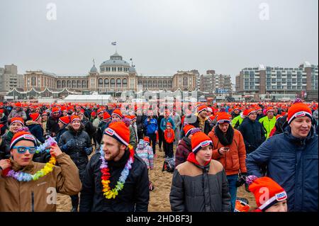 Tausende von Menschen warten mit den traditionellen orangefarbenen Beanies von Unox vor dem traditionellen Neujahrstauchen am Strand von Scheveningen.in dieser Woche sind es genau 25 Jahre seit dem letzten Elfstedentocht-Event (eine fast 200 Kilometer lange Langstrecken-Tour-Skating-Veranstaltung auf Natureis). Es war auch der Tag, an dem die Niederlande erstmals die orangene Eislaufmütze aus Unox kennenlernten. Im Laufe der Jahre wurden Hunderttausende von Unox-Beanies an Besucher und Teilnehmer während Winterveranstaltungen verteilt, wie zum Beispiel beim traditionellen Neujahrstauchen am Strand von Scheven Stockfoto