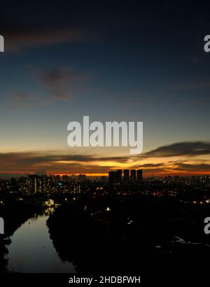 Saigon River bei Sonnenuntergang mit Quận 7 (Bezirk 7) Gebäude / dunkle Silhouetten und beleuchtete Fenster schaffen einen Blick auf die Stadt in HCMC. Stockfoto