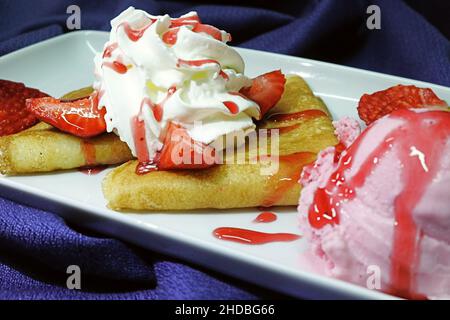 Foto von Crepes mit Schlagsahne und Erdbeer-Belag und Erdbeereis auf einem marineblauen Tuch Stockfoto