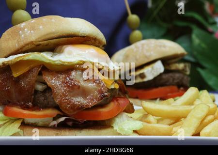 Foto von zwei Sandwiches mit Hamburger und Speck und Pommes frites auf einem marineblauen Tuch Stockfoto