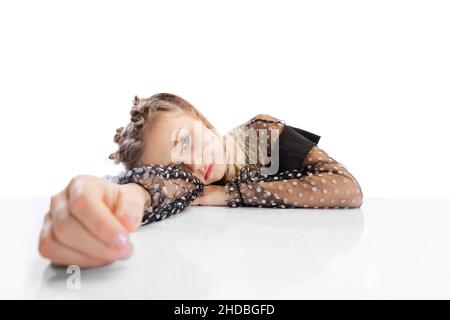 Close-up schöne kleine niedliche Mädchen, Schüler in schwarzem Kleid sitzt am Tisch isoliert auf weißem Studio Hintergrund. Bildung, Kinderkonzept. Stockfoto