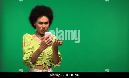 Unzufrieden afroamerikanische Frau mit Smartphone isoliert auf grün Stockfoto