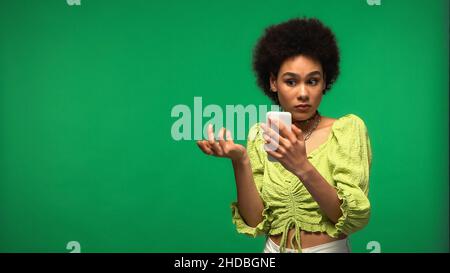 Unzufriedene afroamerikanische Frau mit Smartphone isoliert auf grün Stockfoto