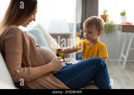 Schwanger Mutter und ihr Kleinkind Sohn verbringen Zeit zusammen zu Hause, kleiner Junge berühren sanft Mutter schwanger Bauch Stockfoto