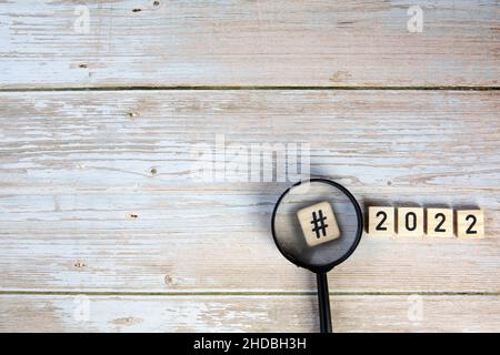 2022 mit Hashtag und Vergrößerungsglas-Konzept auf Holzhintergrund Draufsicht, Kopierraum, Neujahr Stockfoto
