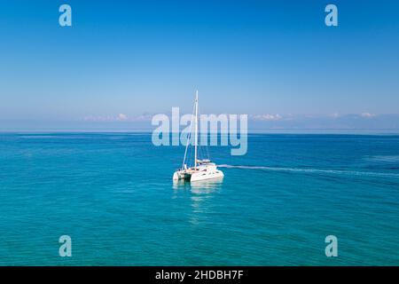 Yacht, die auf dem Mittelmeer Griechenlands driftet und das Boot versteckt, wobei die schaumige Spur unter blauem wolkenlosem Himmel am Horizont zurückbleibt Stockfoto