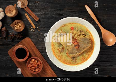 Blick von oben auf Gulai Kambing ist die traditionelle indonesische Hammelcurry-Suppe. Auf Schwarzem Holztisch Stockfoto