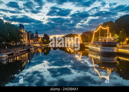 Turku, Finnland - 5. August 2021: Wunderschöner Sonnenuntergang auf dem Aurajoki Fluss mit beleuchteten Schiffen. Stockfoto