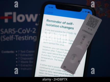 Eine positive laterale Durchflusstestkassette, die neben Empfehlungen der NHS COVID-App auf einem iPhone in London platziert wird. Die britische Gesundheitsbehörde hat gesagt, dass Menschen in England ohne Coronavirus-Symptome, die einen positiven lateralen Flow-Test haben, ab Januar 11 keinen bestätigenden PCR-Test mehr benötigen. Bilddatum: Mittwoch, 5. Januar 2022. Stockfoto