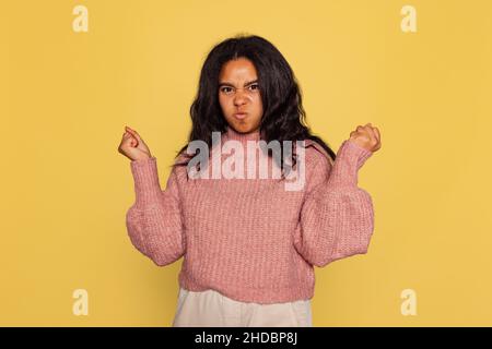 Halblanges Porträt von jungen hübschen dunkelhäutigen Mädchen in warmen Strickpullover auf gelbem Hintergrund isoliert. Stockfoto