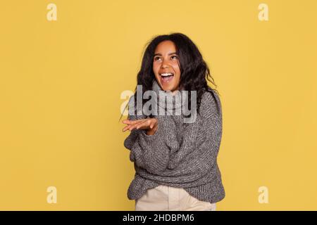 Halblanges Porträt von jungen hübschen dunkelhäutigen Mädchen in warmen Strickpullover auf gelbem Hintergrund isoliert. Stockfoto