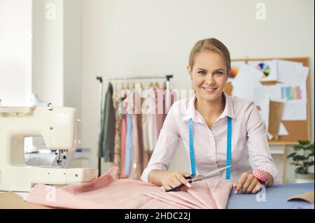 Porträt einer lächelnden, talentierten jungen Näherin an ihrem Arbeitsplatz im Nähstudio. Stockfoto