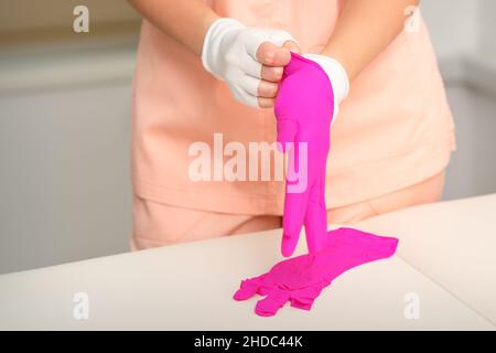 Die Hände der Kosmetikerin tragen die rosa Gummihandschuhe an, um die Kunden zu empfangen Stockfoto