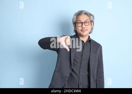 Der erfahrene asiatische Geschäftsmann, der auf dem blauen Hintergrund steht. Stockfoto