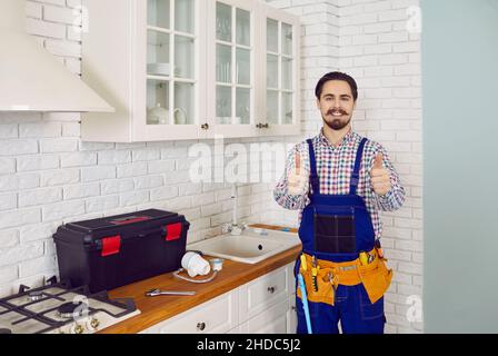 Glücklicher junger Klempner und Reparaturmann garantiert den besten Service und zeigt Daumen nach oben Stockfoto