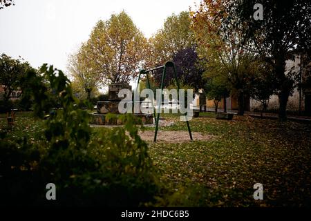Schwingen Sie sich an einem Brunnen zwischen dem Rasen mit bunten Bäumen und im Herbst mit Blättern bedeckt Stockfoto