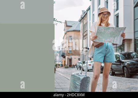 Junge Reisende Frau mit Koffer auf einer sonnigen Stadtstraße. Stockfoto