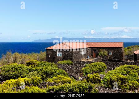 Typisches ländliches Steinhaus aus vulkanischem Gestein auf der Insel Pico mit einem schönen Blick über das Meer und die Insel Sao Jorge, Azoren, Portugal Stockfoto