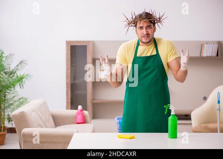 Junger männlicher Auftragnehmer, der auf dem Kopf einen stacheligen Kranz trägt und Hausarbeit leistet Stockfoto