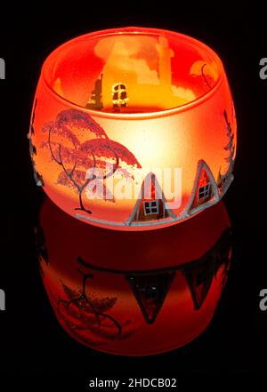 Eine handbemalte Glaskanne mit Winterlandschaft, die von einer Kerze im Inneren der Tasse angezündet wird. Eine Nahaufnahme und die Verwendung von Lichtmalerei. Stockfoto