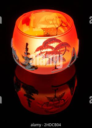 Eine handbemalte Glaskanne mit Winterlandschaft, die von einer Kerze im Inneren der Tasse angezündet wird. Eine Nahaufnahme und die Verwendung von Lichtmalerei. Stockfoto